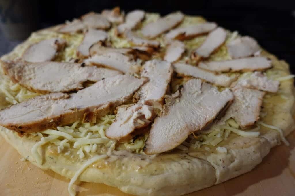 pizza crust with mozzarella cheese and caesar chicken sliced on top