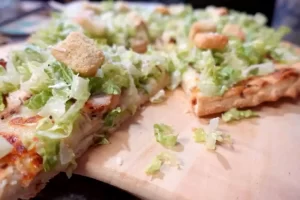 chicken-caesar-salad-pizza-on-pizza-peel-with-slices