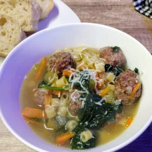 italian wedding soup in a white bowl with homemade bread