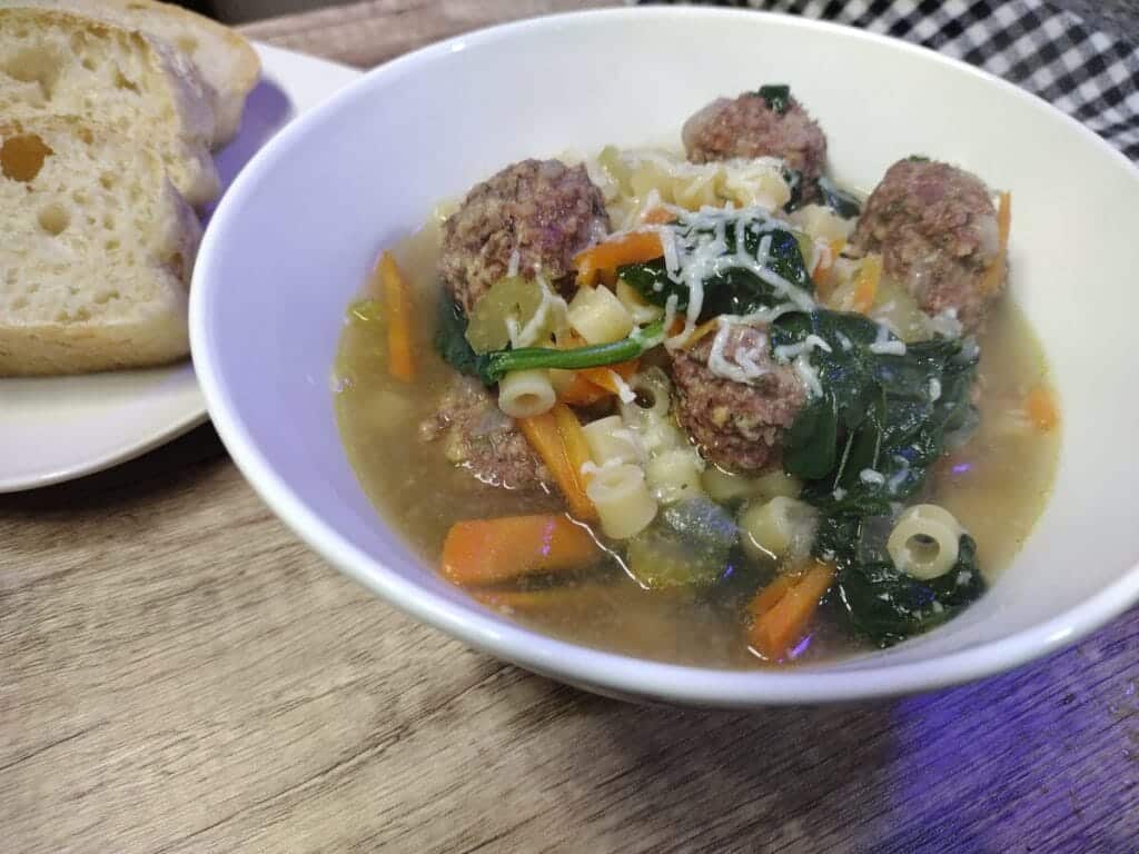 italian wedding soup in a white bowl with homemade bread