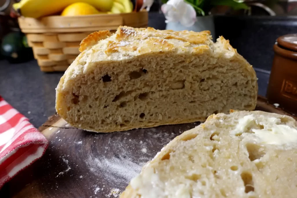 no-knead-bread-showing-buttered-slice-and-loaf-cut-in-half-to-show-soft-bread-with-crispy-crust.