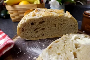 no-knead-bread-showing-buttered-slice-and-loaf-cut-in-half-to-show-soft-bread-with-crispy-crust.