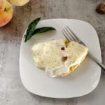 peach cobbler on white plate with fork and peaches along side