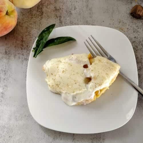 peach cobbler on white plate with fork and peaches along side