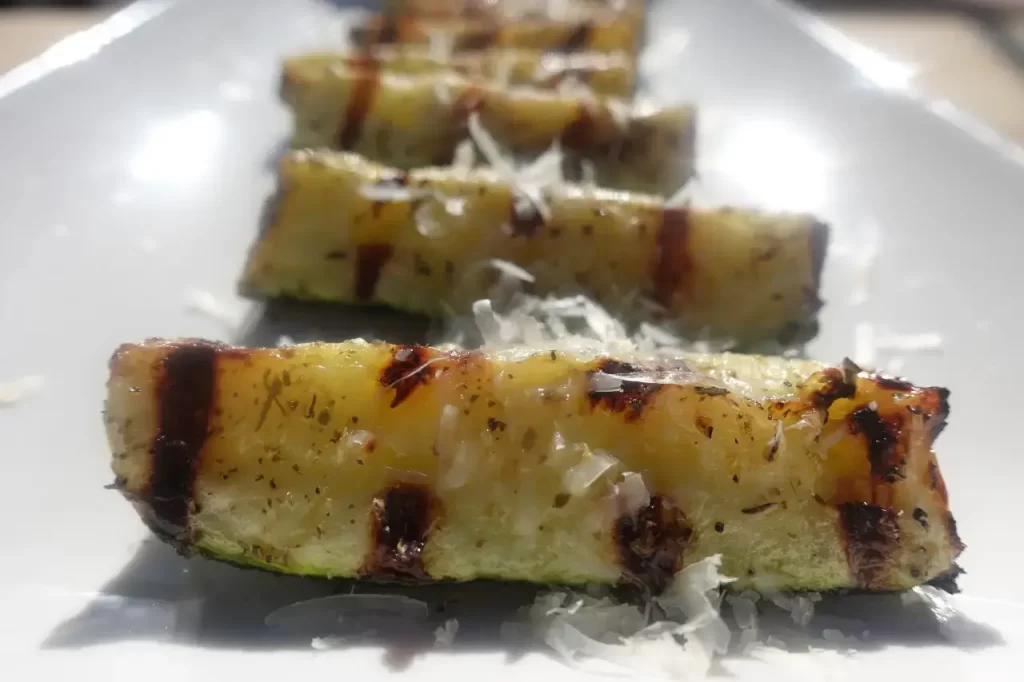 grilled zucchini spears on white plate with grated parmesan cheese