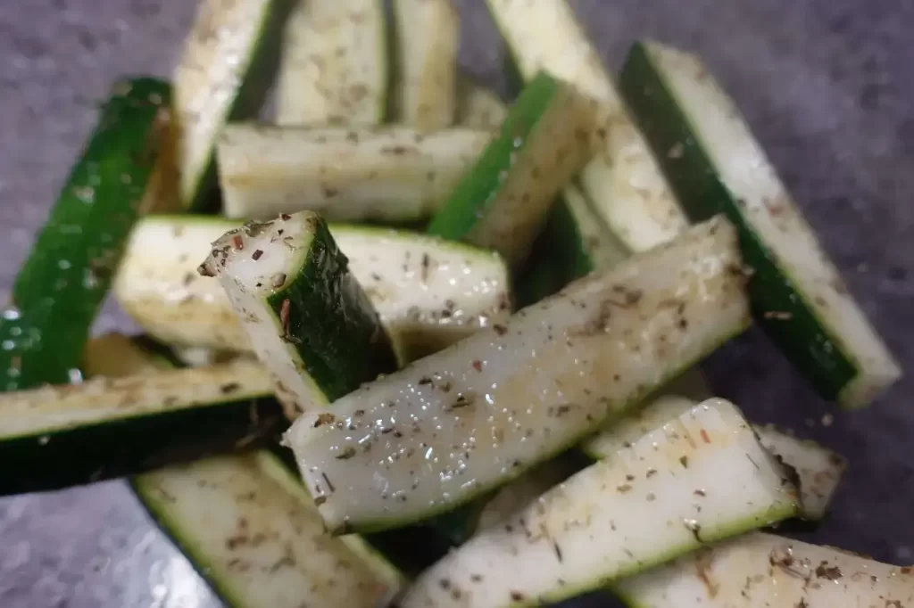 zucchini spears in bowl tossed with italian season and olive oil