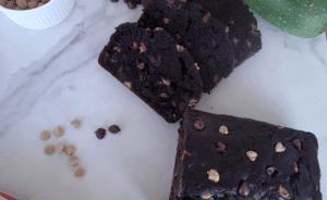 chocolate zucchini bread with chocolate chips and peanut butter chips. both peanut butter chips and chocolate chips alongside the bread on a white plate.