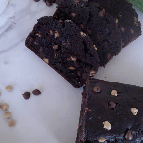 chocolate zucchini bread with chocolate chips and peanut butter chips. both peanut butter chips and chocolate chips alongside the bread on a white plate.