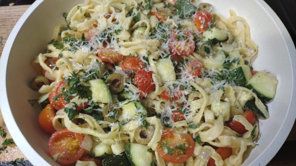 pasta with zucchini and tomatoes in white serving dish