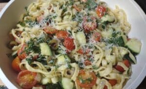 pasta with zucchini and tomatoes in white serving dish