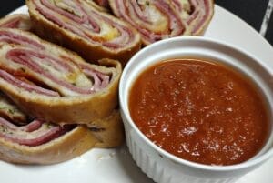 stromboli sliced on white plate with marinara sauce in white bowl