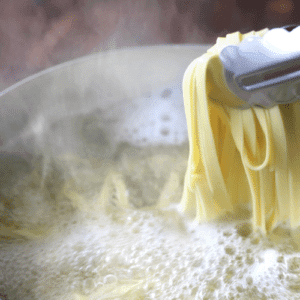 homemade pasta boiling in water .  tongs holding cooked noodles.