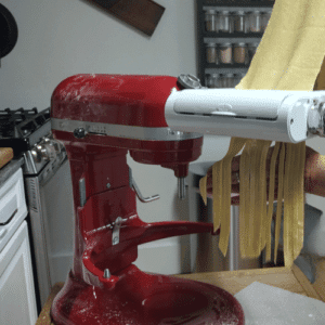 red kitchen aid stand mixer with pasta attatchment running homemade pasta noodles through it