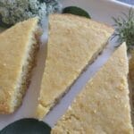 wedges of cornbread on a white tray with sage and parsley seed heads