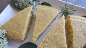 wedges of cornbread on a white tray with sage and parsley seed heads