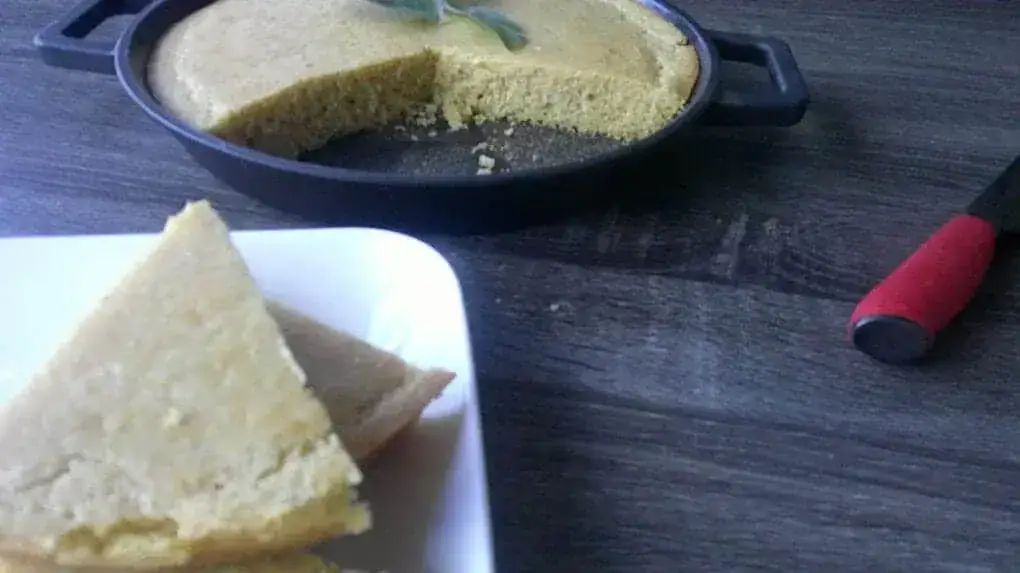 cornbread wedge on white plate with pan of cornbread in background