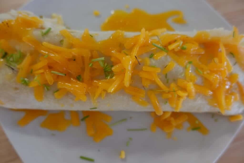 cheesy chicken enchilada on a white plate sprinkled with cheddar cheese and chives