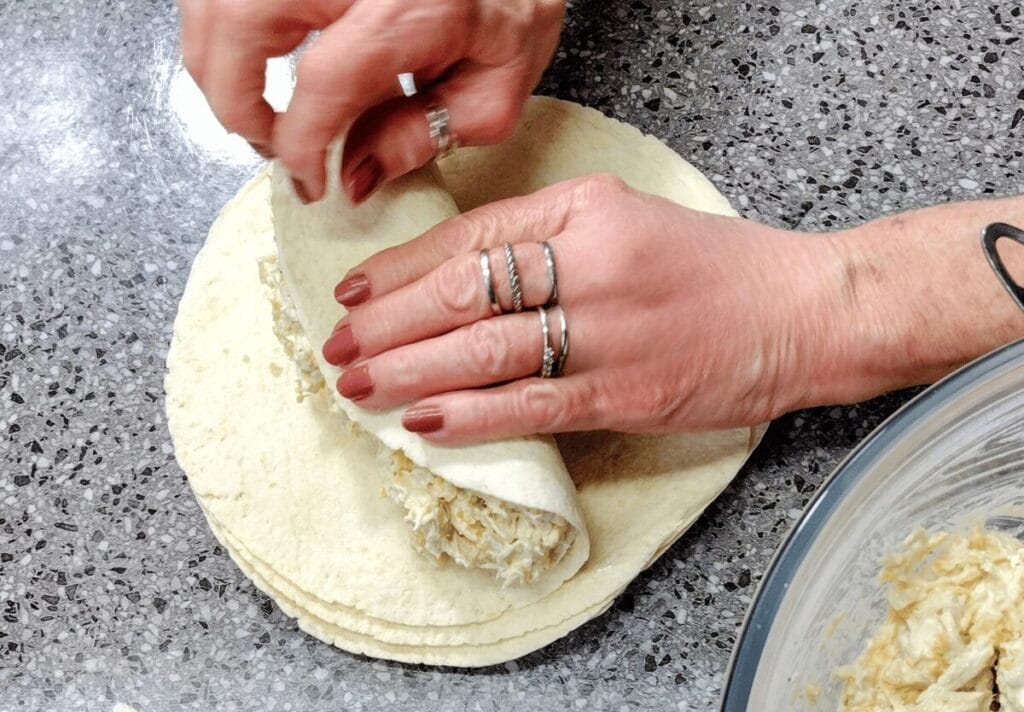 rolling up cheesy chicken enchiladas