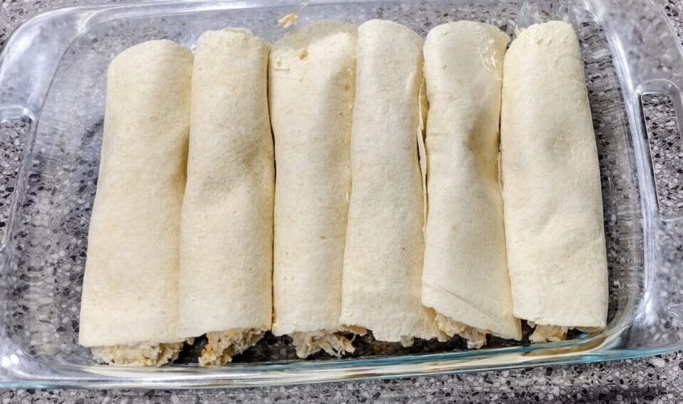 cheesy chicken enchiladas rolled in clear baking dish