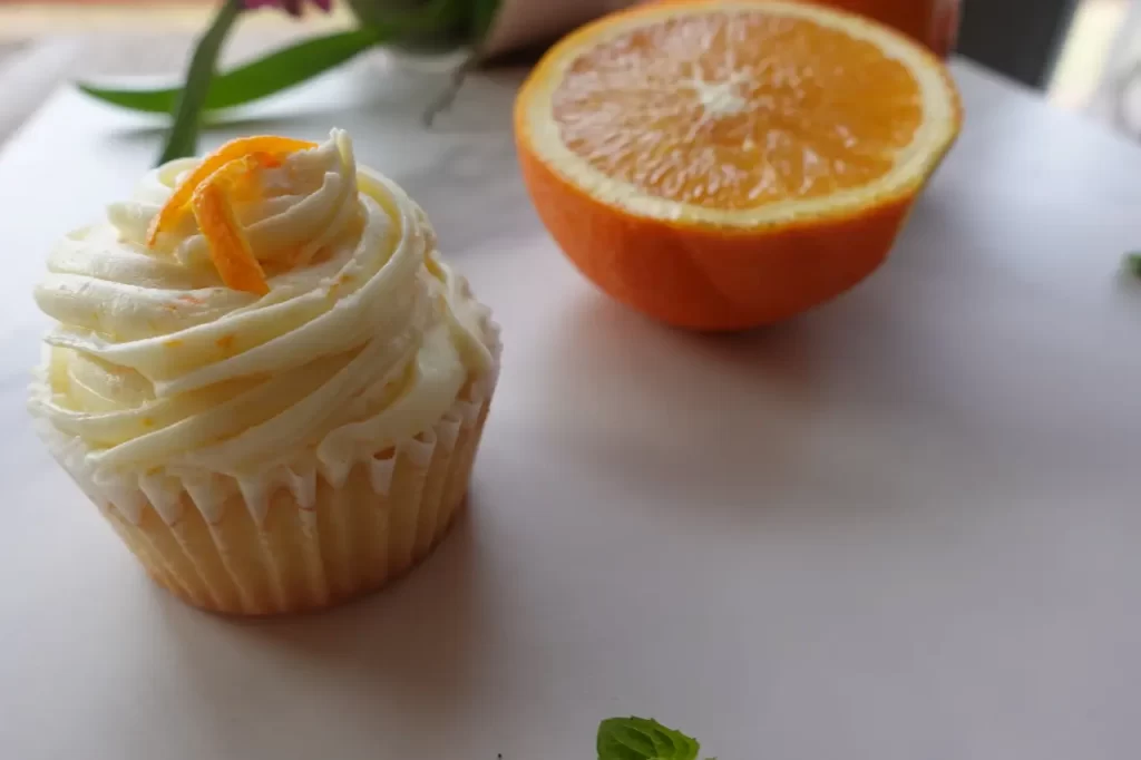 orange creamsicle cupcake on marble countertop with 1/2 an orange