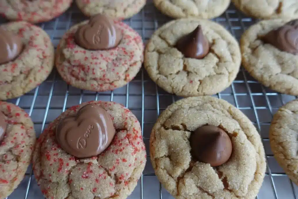 peanut butter blossoms cookies on rack with chocolate hearts and red sugar and hershey kisses white sugar