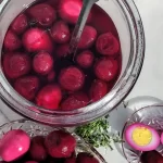 pickled eggs in a jug and on a serving tray and 1 cut in 1/2