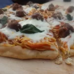 spaghetti and meatball pizza recipe on wooden peel