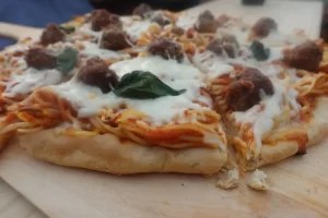 spaghetti and meatball pizza recipe on wooden peel