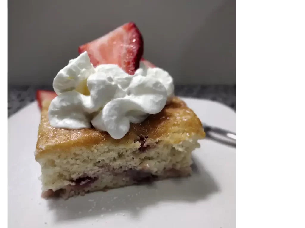 strawberry cake on white plate with whipped topping and fresh strawberries