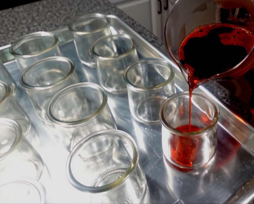 pouring red jello into 5 oz cups for layered jello cup recipe