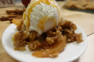 apple crisp on white plate with vanilla ice cream and caramel sauce