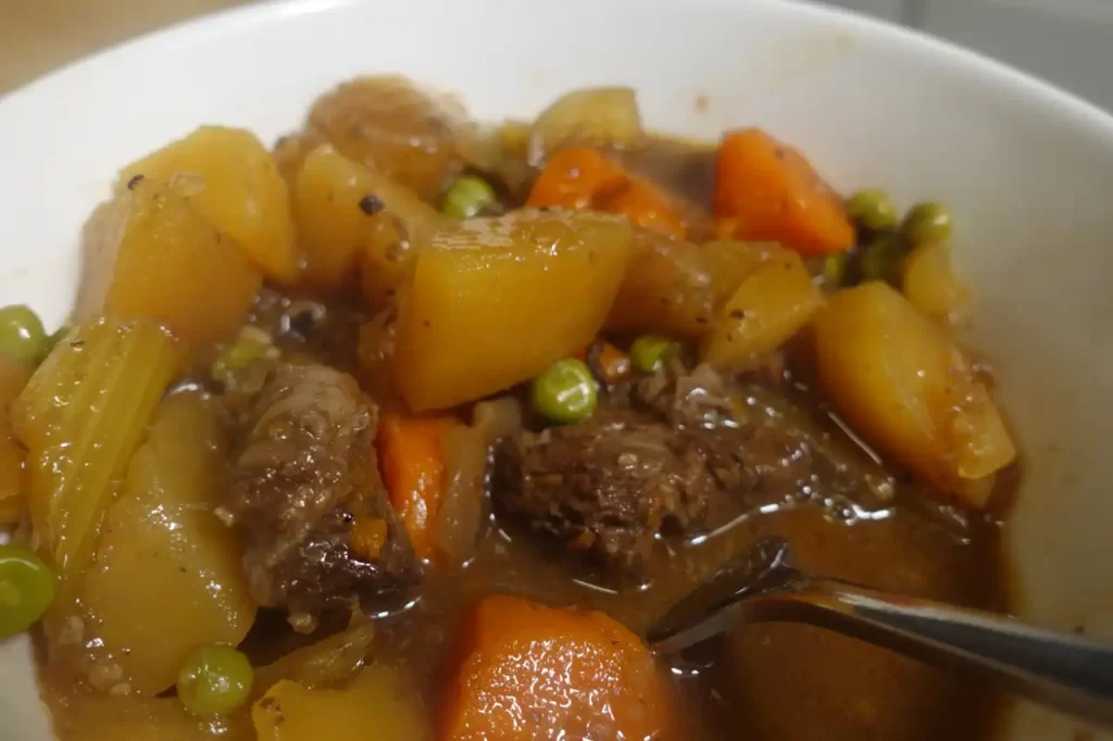 beef stew with carrots, beef, potatoes and onions and peas in serving dish