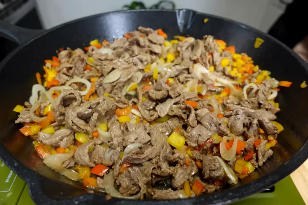 side-view-steak-onions-peppers-in-cast-iron-skillet.