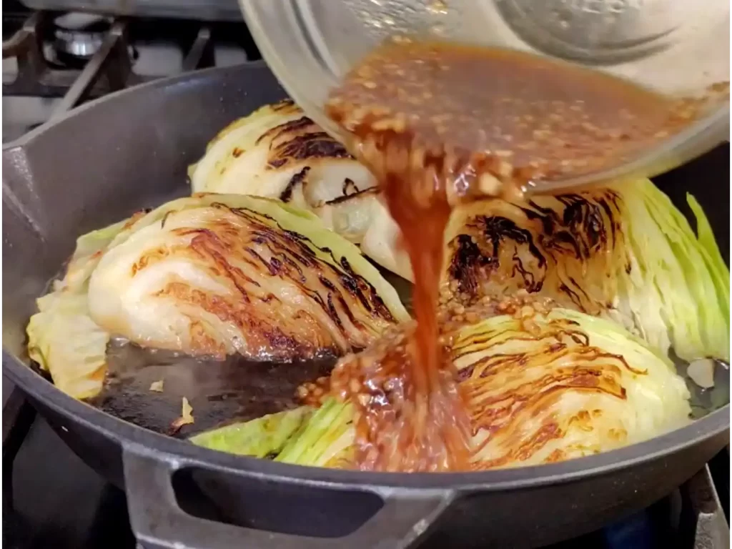 sweet-garlic-chili-cabbage-in-cast-iron-skillet-being-drizzled-with-chili-sauce