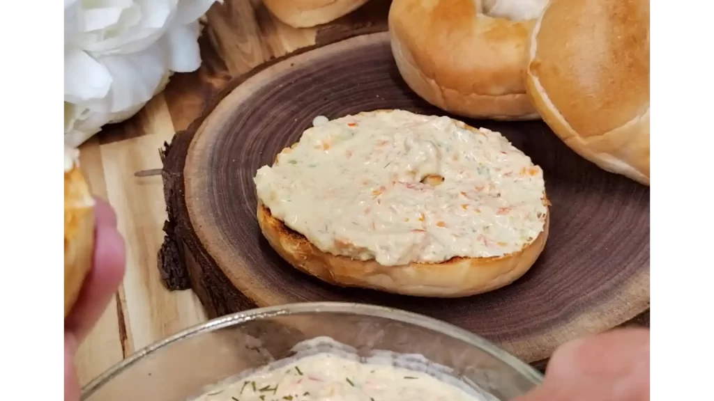 veggie-cream-cheese-bagel-on-wooden-plate-with-bagels-in-background