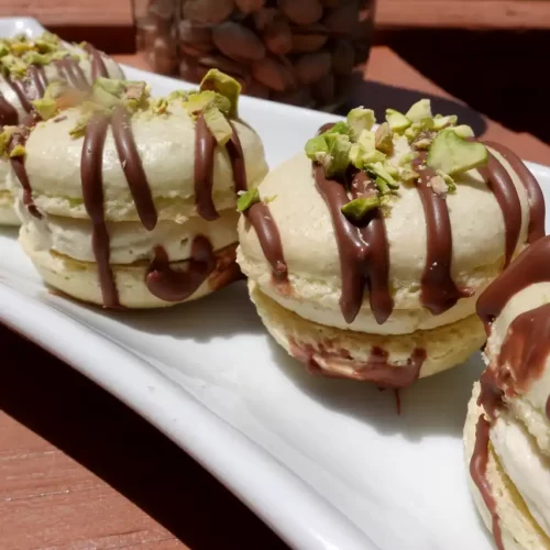 pistachio-cream-macarons-on-white-tray-drizzled-with-chocolate-and-salted-pistachios.