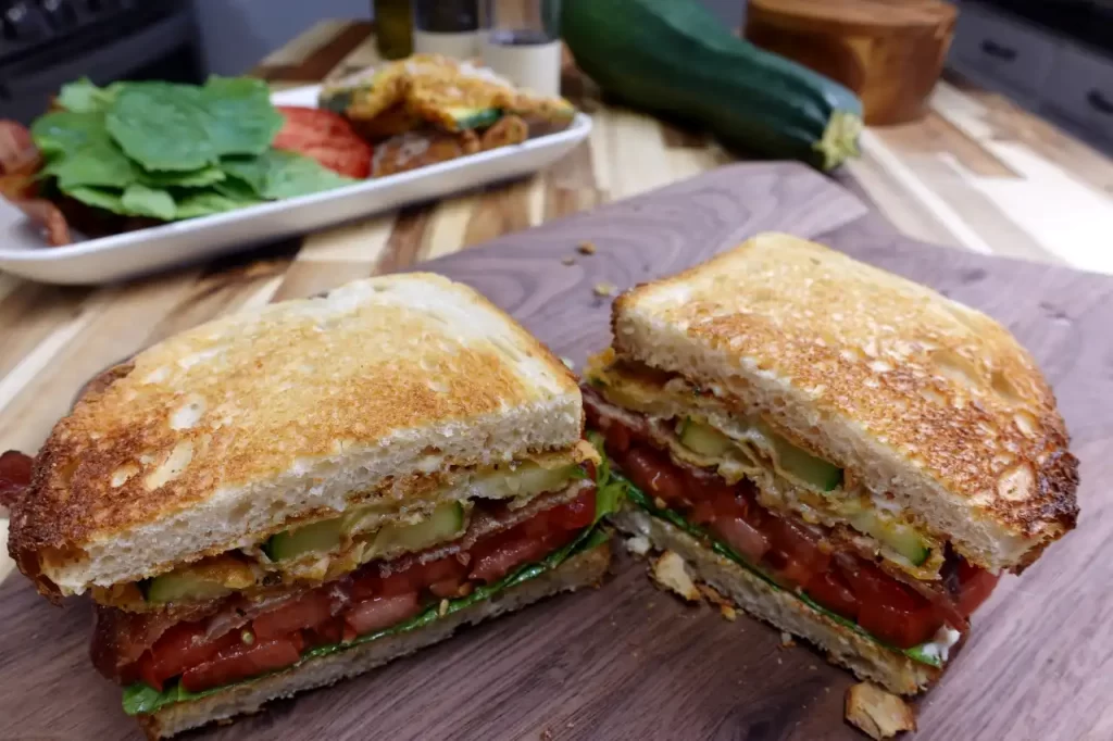 crispy-fried-zucchini-blt-cut-in-half-with-whole-zucchini-in-background.webp