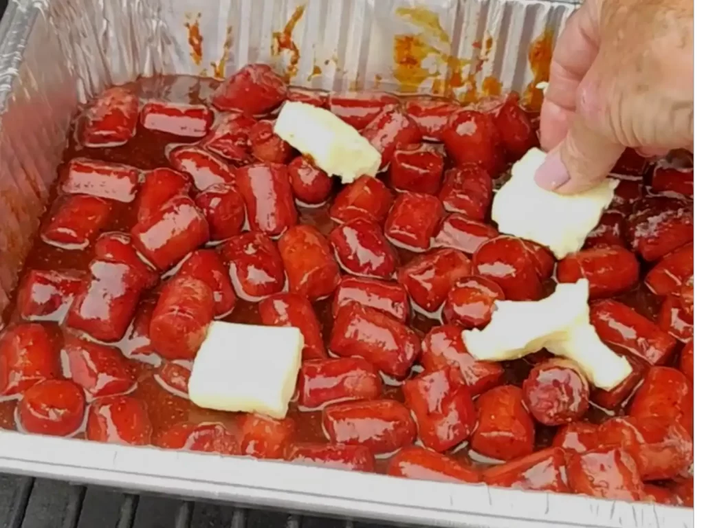 placing-butter-pats-on-burnt-end-hot-dogs-on-grill
