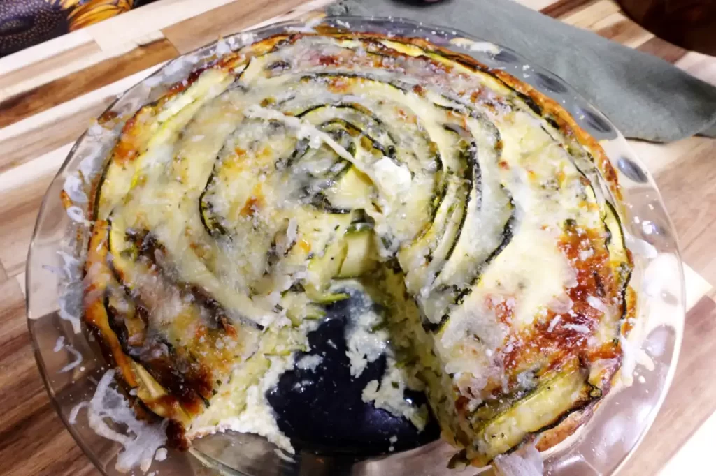 Crustless-zucchini-rose-pie-with-a-slice-removed-showing-layers-of-thin-zucchini-ribbons-and-creamy-cheese-filling