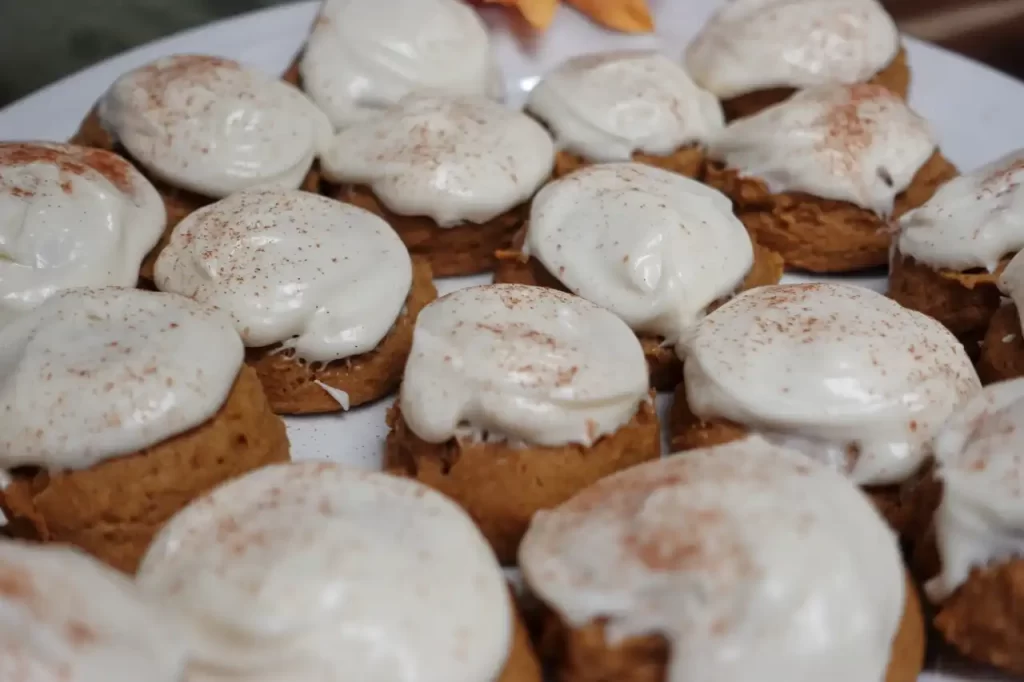 Pumpkin-cookies-with-cream-cheese-frosting-arranged-on-a-white-plate.