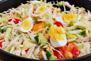 Mediterranean-chopped-cabbage-salad-in-a-black-bowl-with-shredded-cabbage-hard-boiled-eggs-chickpeas-cucumbers-tomatoes-green-olives-and-homemade-vinaigrette