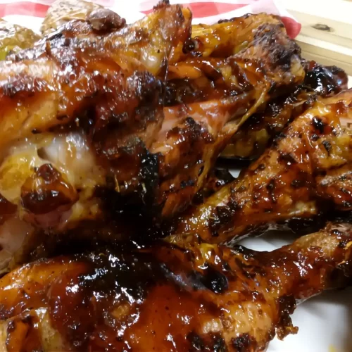Traeger-smoked-chicken-drumsticks-coated-in-glossy-BBQ-sauce-served-on-a-white-platter-with-golden-roasted-potatoes